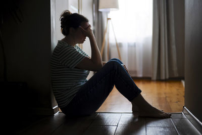 Side view of woman sitting on hardwood floor at home