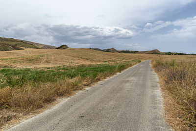 Dirt road amidst field against sky