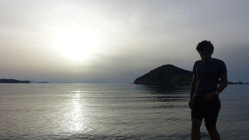 Rear view of man standing at beach against sky