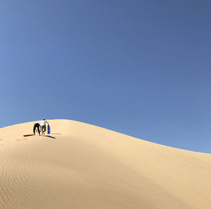 Low angle view of people walking at desert against clear blue sky