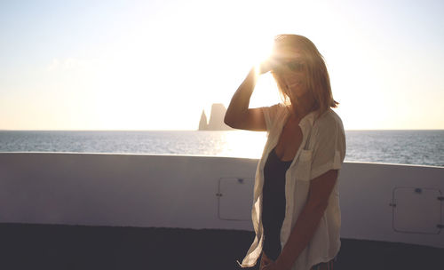 Portrait of smiling young woman standing in cruise ship against clear sky during sunset