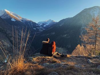 Rear view of men sitting on mountain against sky