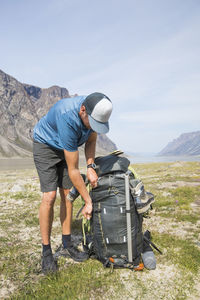 Hiker leans over to zip up backpack his large, heavy backpack.