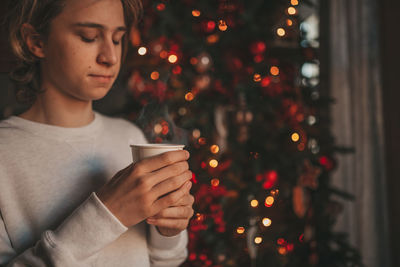 Portrait of candid authentic smiling handsome boy teenager using mobile phone at xmas home interior