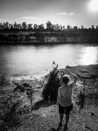 Rear view of boy photographing by lake against sky