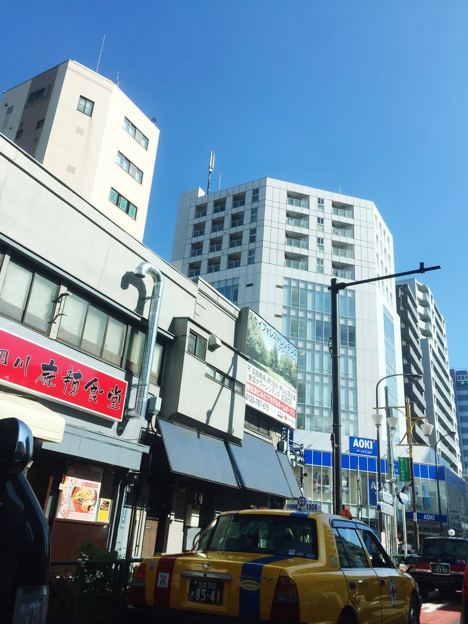 building exterior, architecture, built structure, city, low angle view, clear sky, transportation, car, mode of transport, skyscraper, modern, land vehicle, office building, tall - high, tower, building, city life, road signal, communication, blue