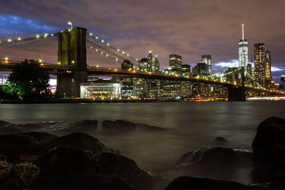 Illuminated bridge over river against sky in city at night