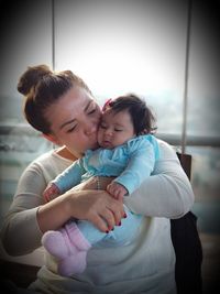 Mother kissing cute daughter while sitting at home