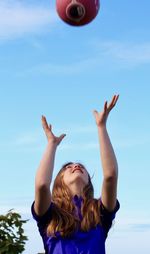 Low angle view of young woman playing with ball against clear sky