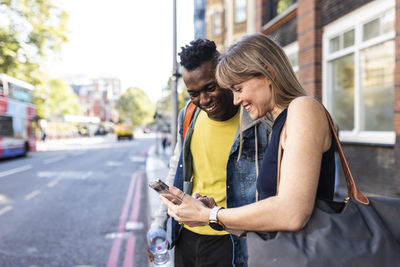 Smiling woman sharing smart phone with friend standing at street