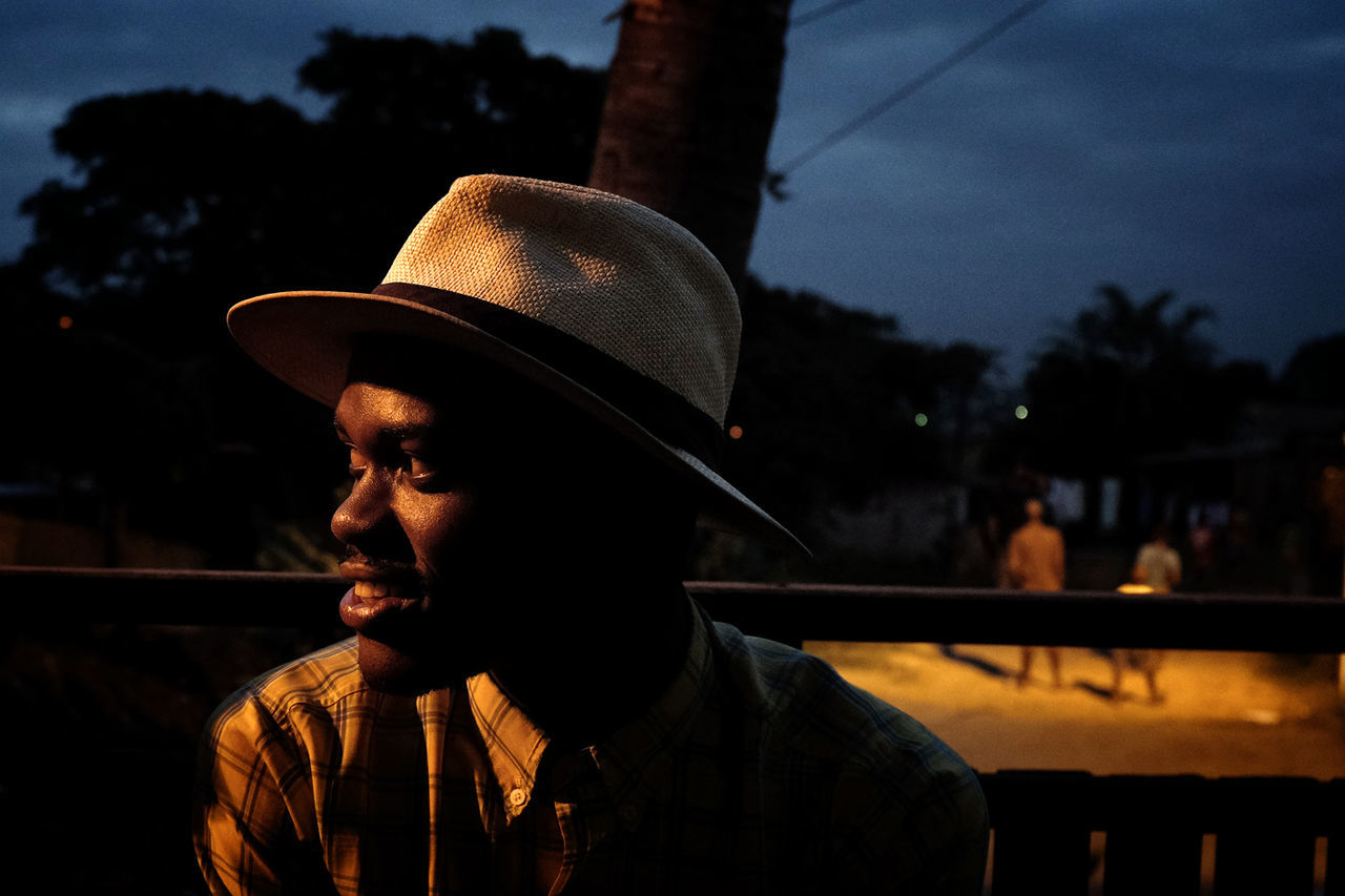 hat, real people, one person, headshot, leisure activity, lifestyles, focus on foreground, clothing, men, portrait, looking, young men, incidental people, nature, tree, young adult, sunlight, outdoors, looking away, contemplation