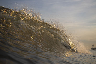 Waves splashing in sea against sky at sunset