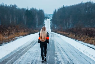 Rear view of woman walking on snow covered road