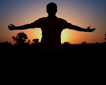 Silhouette man with arms outstretched against sunset sky