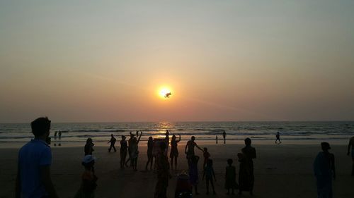 People on beach against sky during sunset