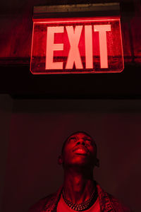 Low angle portrait of young man standing against illuminated sign