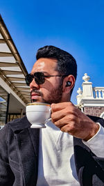 Portrait of man holding coffee cup against sky