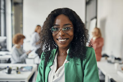 Portrait of a smiling businesswoman in office with colleagues in background