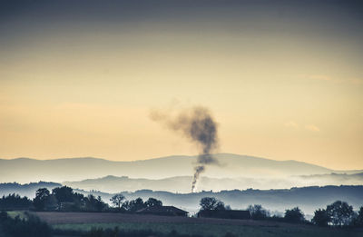 Smoke emitting from factory against sky at sunset