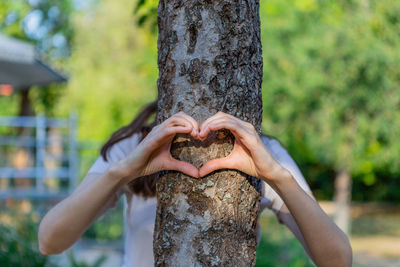 Women's hands show the heart in front of the tree trunk.