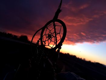 Close-up of silhouette dreamcatcher against cloudy sky at sunset