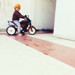 Side view of cute boy with turban sitting on toy motorcycle outside house