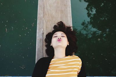 Portrait of beautiful young woman protruding while lying on wood over lake