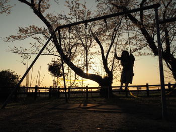 Silhouette woman standing by tree against sky during sunset