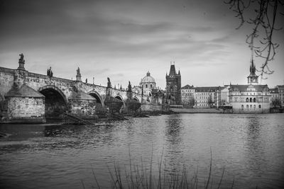 Bridge over river by buildings against sky