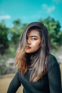 Portrait of young woman standing against trees