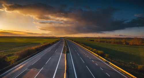 Road passing through field against sky at sunset