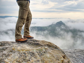 Low section of man standing on rock against sky