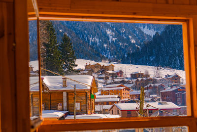 Scenic view of snow covered trees by buildings against mountain