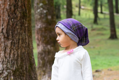 Girl looking away while standing by tree trunk