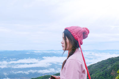 Side view of woman standing on mountain peak against cloudy sky