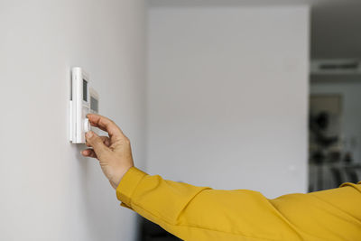 Mature woman adjusting thermostat in living room
