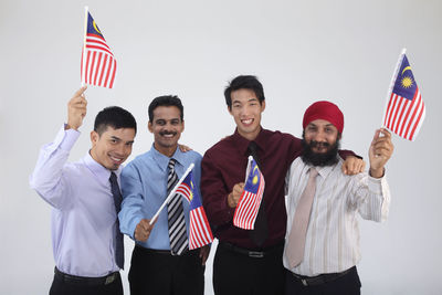 Portrait of smiling businessmen holding malaysia flags against gray background