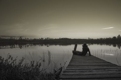 Man sitting on pier over lake against sky
