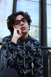 Young man looking away while sitting on window