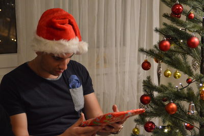 Man in santa hat by christmas tree holding present