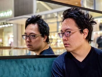 Young asian man in eyeglasses looking into mirror above bench.