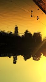 Silhouette birds flying over lake against sky during sunset