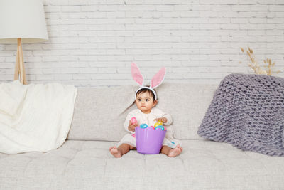 Portrait of young woman sitting on sofa against wall