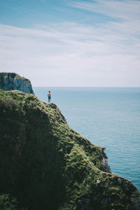 Man standing on cliff by sea against sky