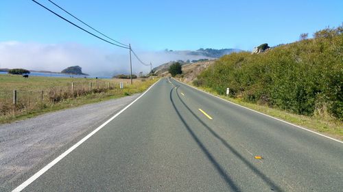 Country road passing through foggy rural landscape against sky