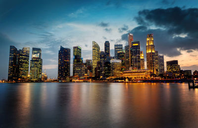 Illuminated modern buildings by bay against sky