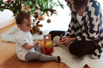 Mother playing with baby by christmas tree at home