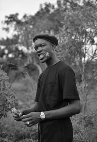 Portrait of young man with flower in mouth standing against trees