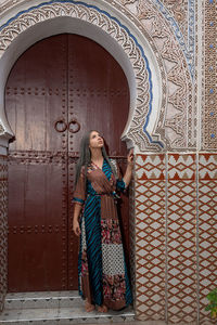 Woman looking away while standing against door of building