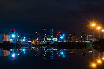 Illuminated city by river against sky at night